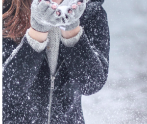 Hands of a person in a black winter coat holding snow in fingerless mittens.